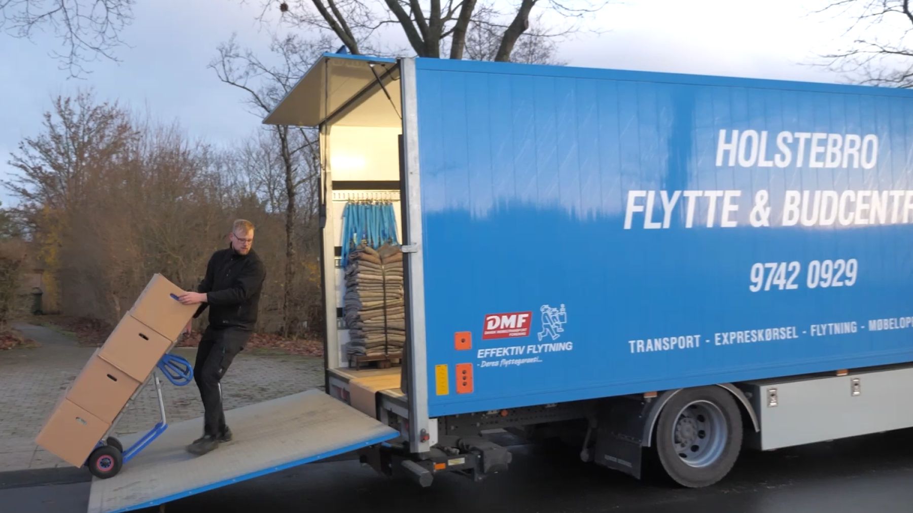 Flyttemand kører flyttekasser op ad rampen til en blå HOFBUD-lastbil